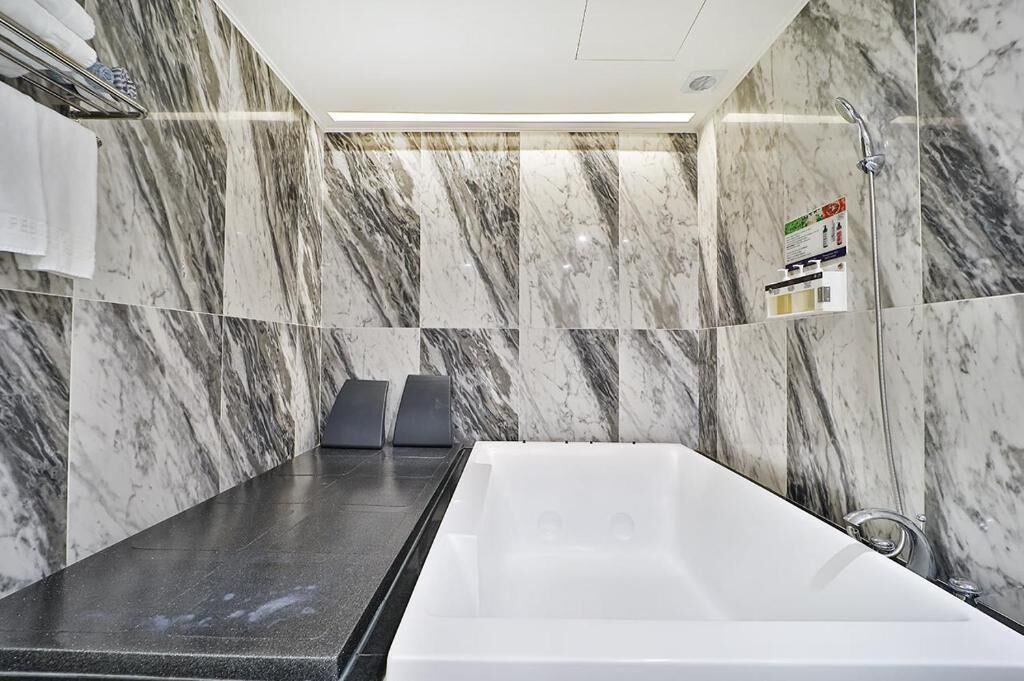 A modern bathroom with a large white bathtub, marble walls, and a shower area.