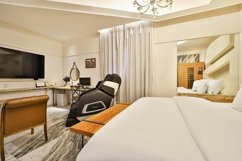 A hotel room with a bed, a desk with a computer, a chair, a TV, and a mirror.