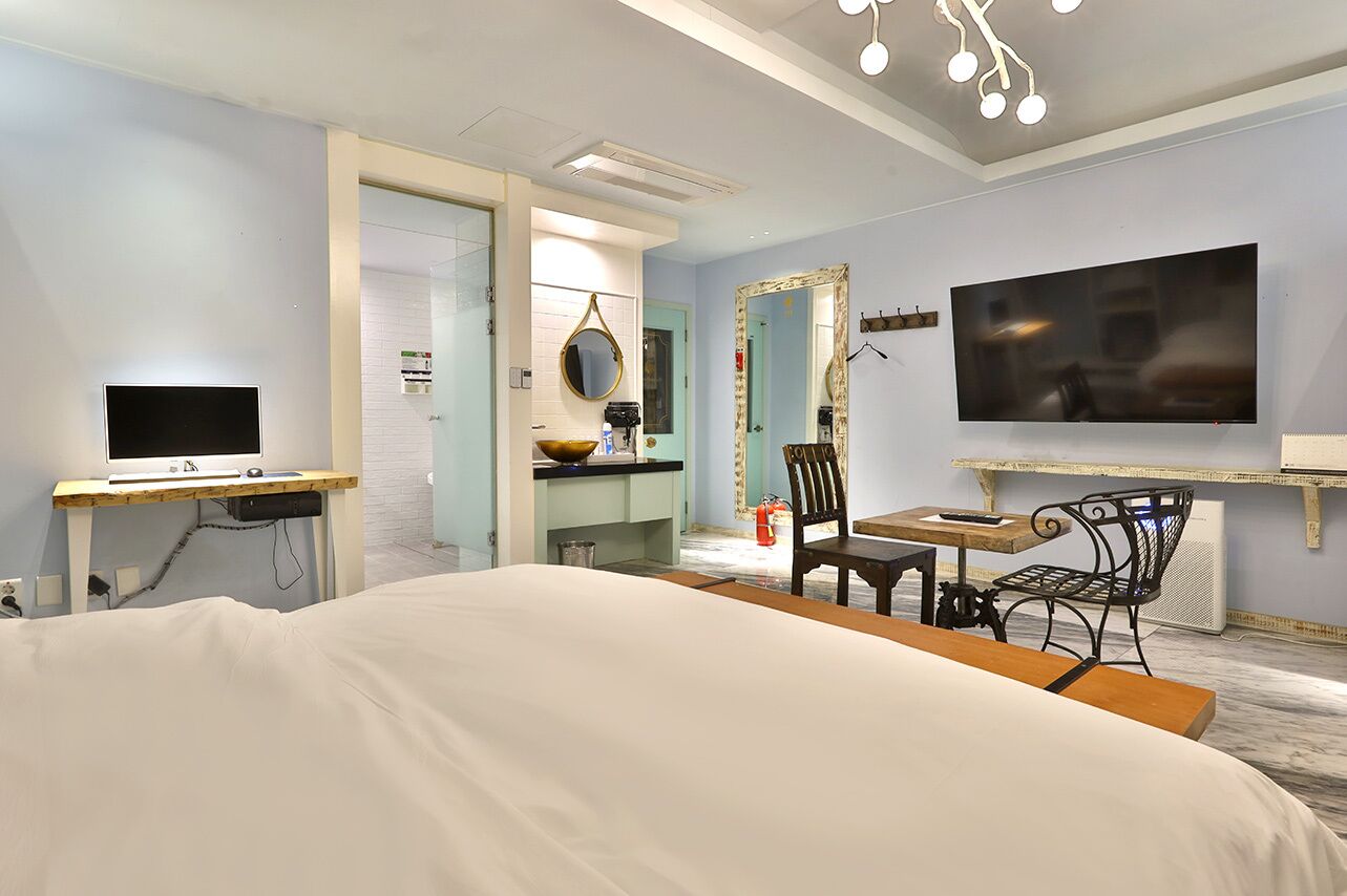 A bedroom with a bed, a desk, a chair, a TV, and a bathroom visible through an open door.