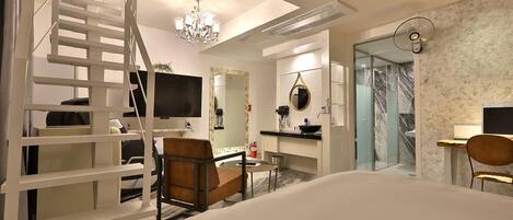 Una habitación de hotel moderna con cama, escritorio, silla, una mesita, espejo, candelabro y una escalera.