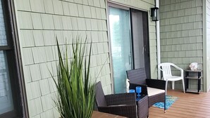 A covered patio area with a wooden table and chairs, a potted plant, and a sliding glass door leading to an outdoor space. - Exquisite 2 Bedroom/2 Bathroom - Walk to Beach and Boardwalk (Ocean City)