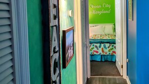 A hallway with green walls, a bed with a colorful bedspread, and a sign that reads "Ocean City Maryland". - Exquisite 2 Bedroom/2 Bathroom - Walk to Beach and Boardwalk (Ocean City)