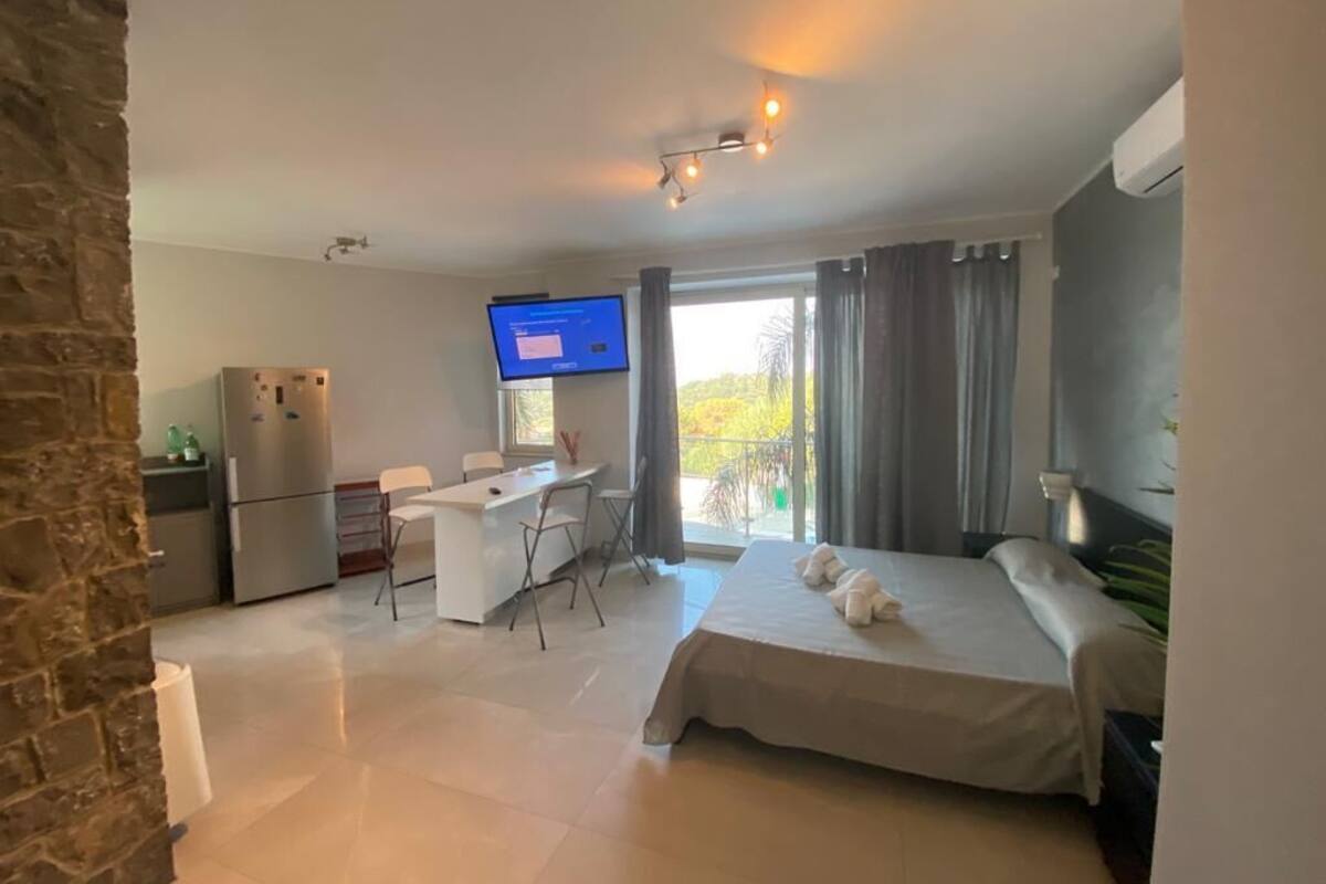 A modern hotel room with a bed, a desk, a television, and a balcony with curtains.