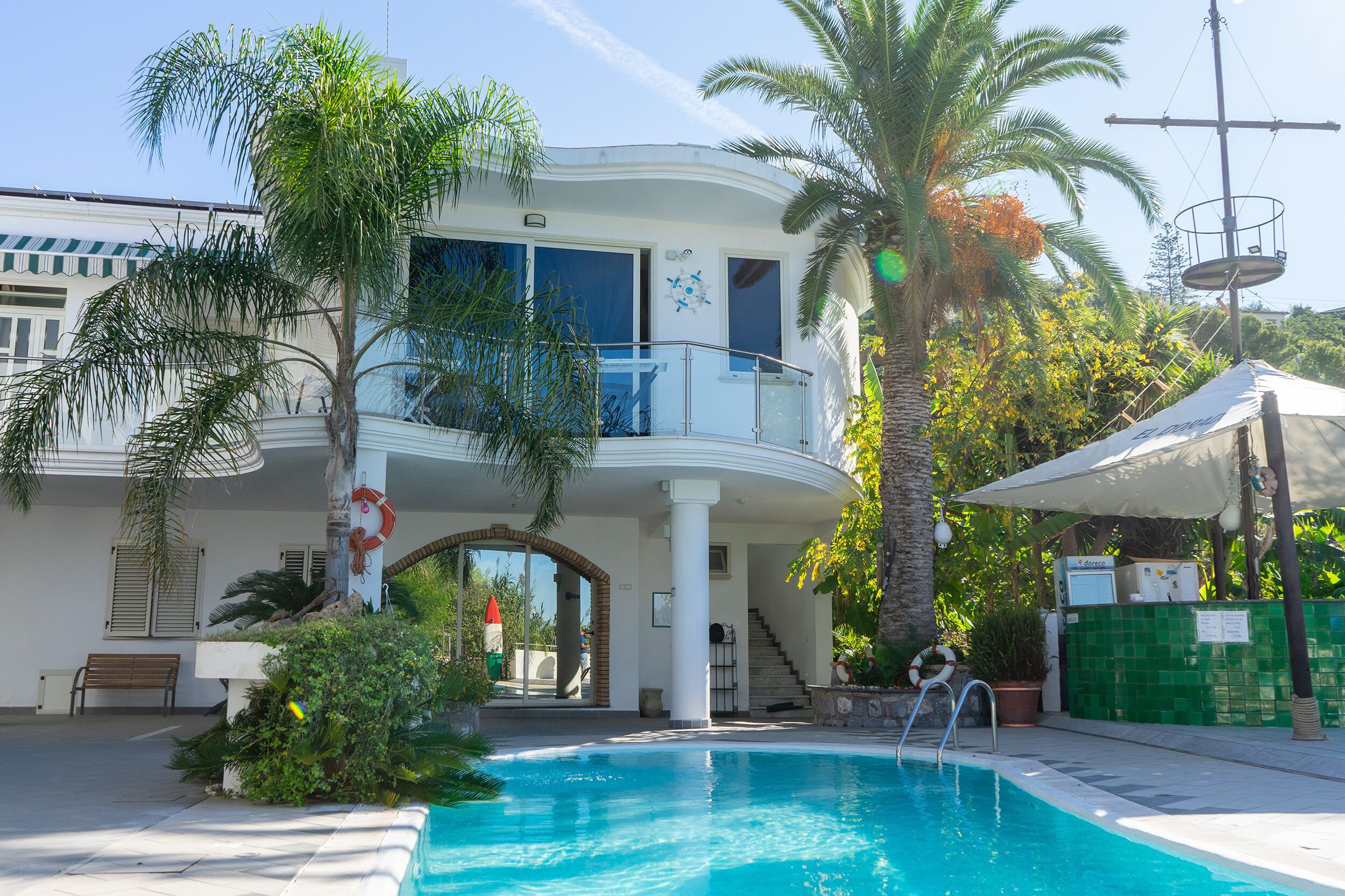 A two-story building with a swimming pool, palm trees, and a balcony.