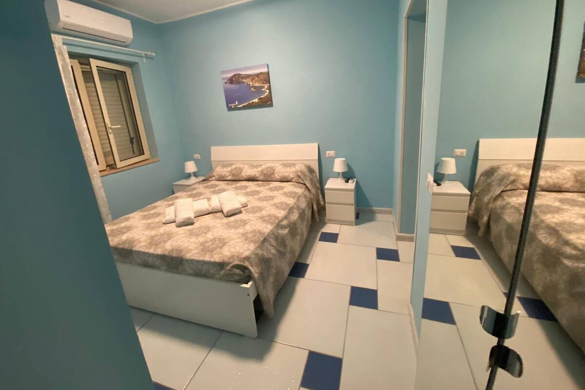 A bedroom with a bed, bedside tables, a window, and a wall-mounted air conditioner.