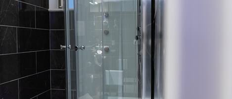 A modern bathroom with black marble tiles, a glass-enclosed shower, and a visible toilet.