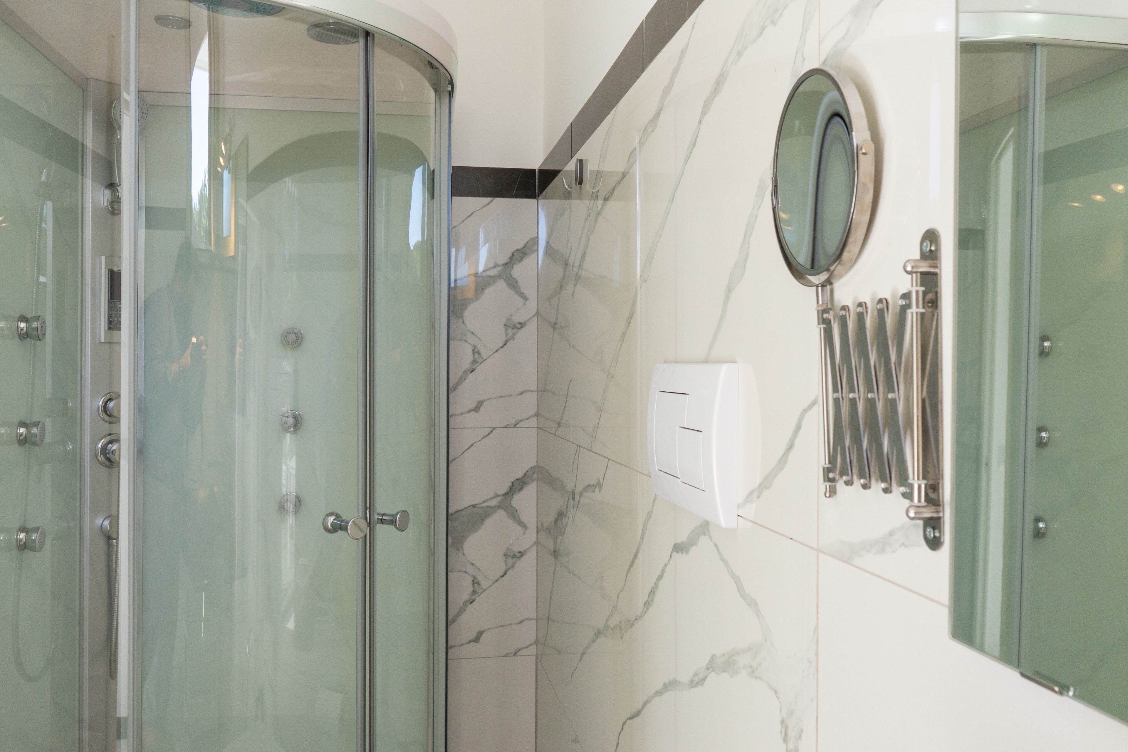 A modern bathroom with a glass-enclosed shower, marble walls, and a mounted towel rack.