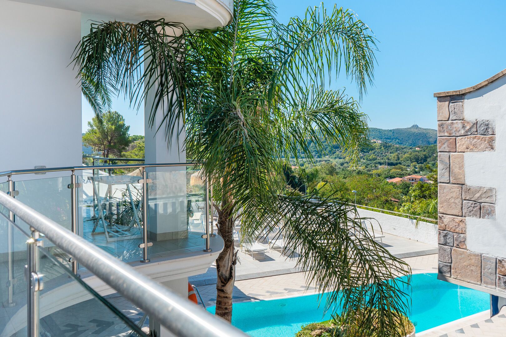Varanda com guarda-corpo de vidro, vista para piscina e para o campo.