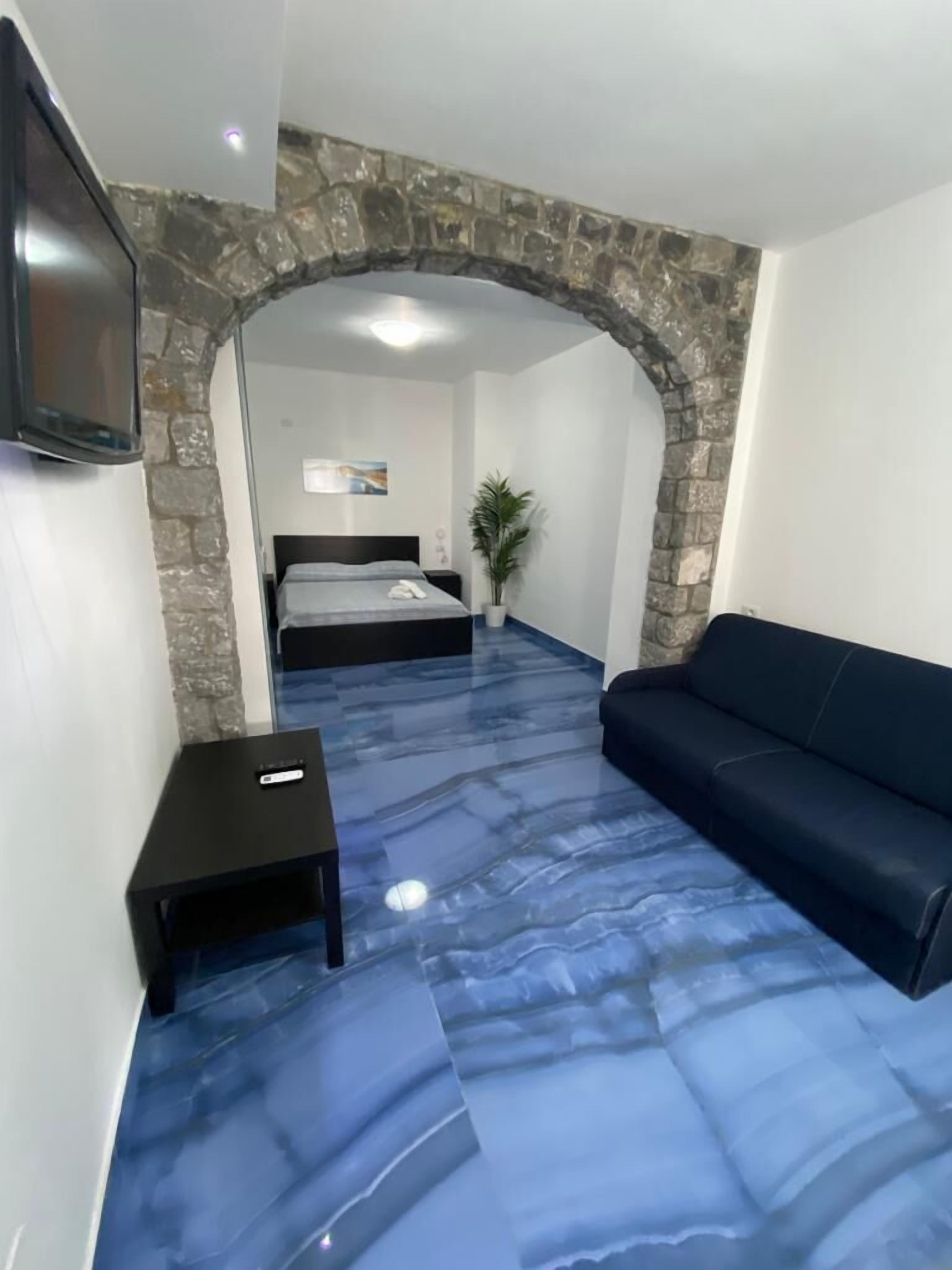 A room with a stone archway, a bed with a blue mattress, a black sofa, and a small table with a remote control.