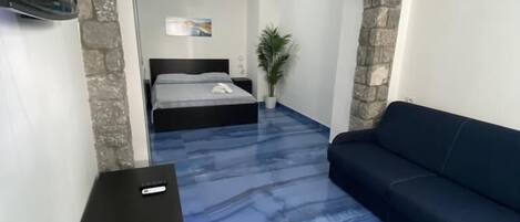 A room with a stone archway, a bed with a blue mattress, a black sofa, and a small table with a remote control.