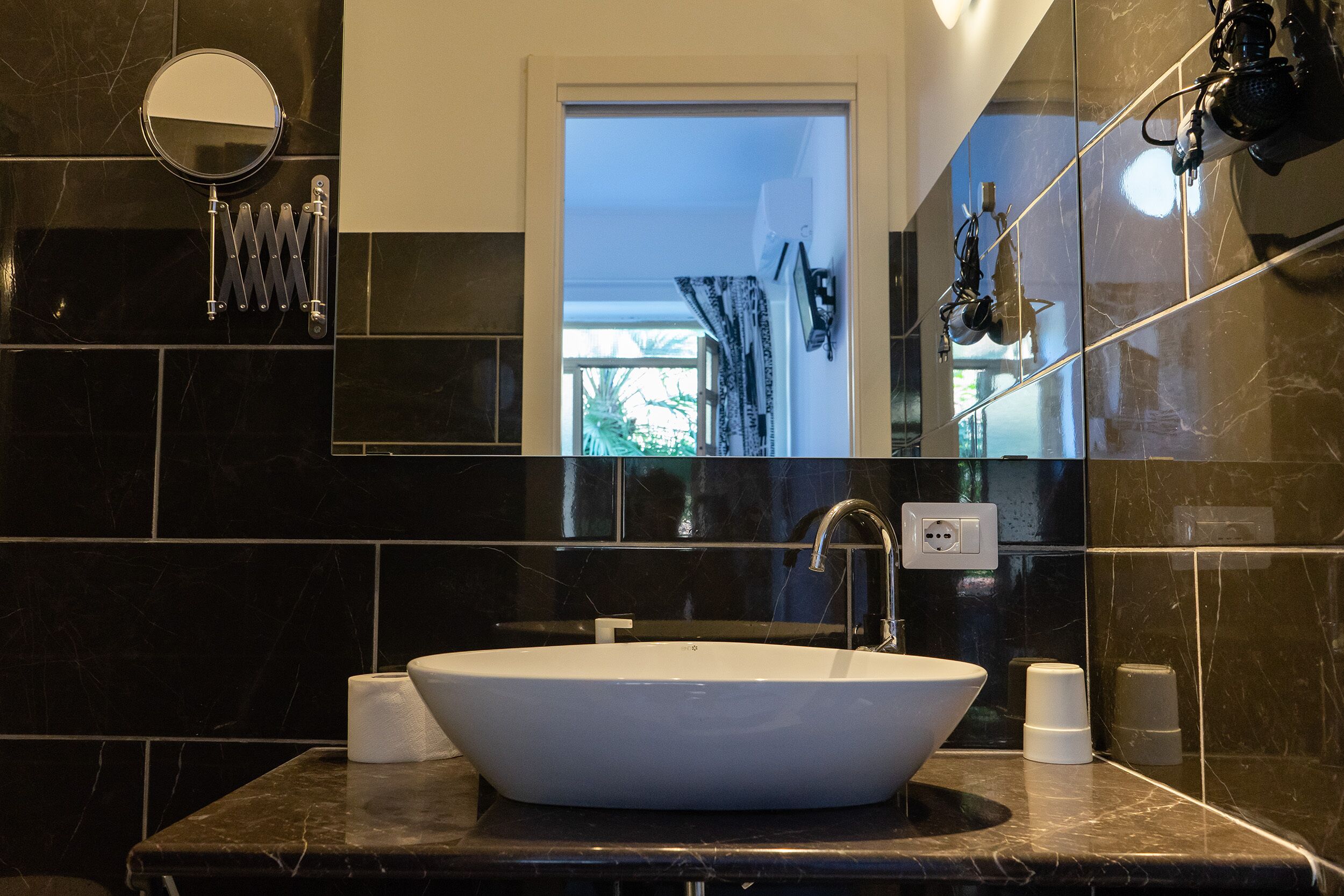 A bathroom with a white sink, black marble tiles, a mirror, and a towel rack.