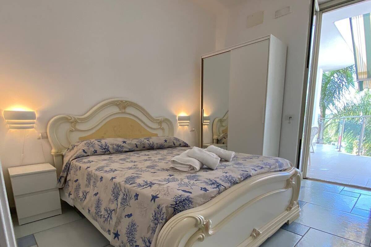 A bedroom with a bed, bedside tables, a mirror, and a view of the outdoors.