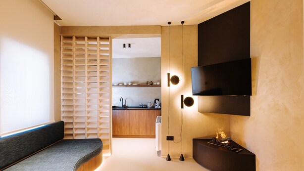 A modern interior with a built-in bench, a fireplace, and a kitchen area visible through a sliding door.