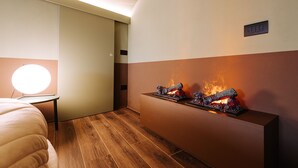 Ein modernes Hotelzimmer mit Holzboden, einem Bett, einem Nachttisch mit Lampe und einem an der Wand montierten Kamin.