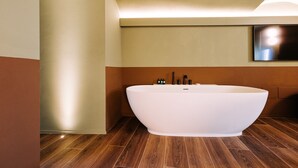 Ein modernes Badezimmer mit freistehender Badewanne, Holzboden und einem wandmontierten Flachbildfernseher.