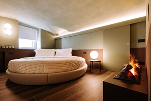 Ein modernes Schlafzimmer mit einem runden Bett, einem kleinen Nachttisch, einer Wandleuchte und einem Kamin.
