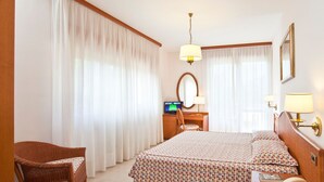 A hotel room with a bed, a desk with a computer, a chair, and a bedside table with a lamp and a phone. - Hotel Gabbiano by Double Hospitality (Garda)
