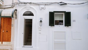 Un edificio blanco con una puerta de madera, una ventana con contraventanas verdes y un letrero con el número 15.