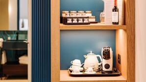 A wooden cabinet with shelves containing jars, a bottle, a teapot, cups, and a coffee maker. - Suite Queen Room 2 maggio (Monopoli)