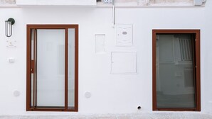 Edifici blanc amb dues portes, una amb panell de vidre i una altra amb reixatge metàl·lic, i una petita unitat de ventilació a la paret.
