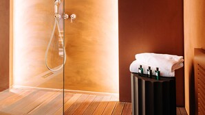 Una sala de spa amb sòl de fusta, una separació de vidre, una zona de dutxa i un penjador de tovalloles amb ampolles.