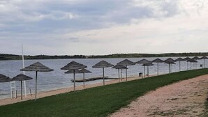 A beach with rows of umbrellas and a path along the water. - Sunrise Monsaraz Blue - Casa com 2 Quartos Jardim (Évora)