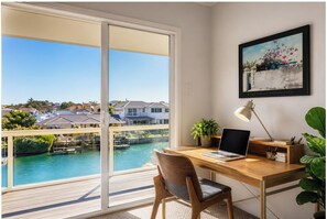 A room with a desk, chair, laptop, lamp, and a painting on the wall. - Waterfront Canal Retreat | Jetty, Kayaks & Dolphin (Halls Head)