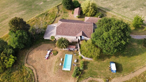 Vista aérea de una propiedad con piscina, una casa grande con techo de tejas y follaje circundante.