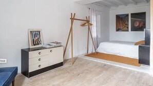 Un dormitorio con cama, cómoda, perchero de madera y un cuadro en la pared.