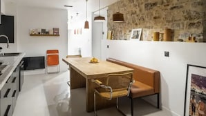 Una cocina moderna con una isla central, un comedor con banco y silla, y una pared de piedra con obras de arte.