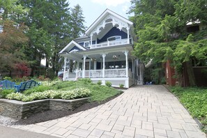 A two-story house with a porch, surrounded by greenery and trees.