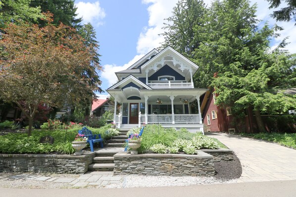 A two-story house with a porch, surrounded by a garden with various plants and a stone wall.