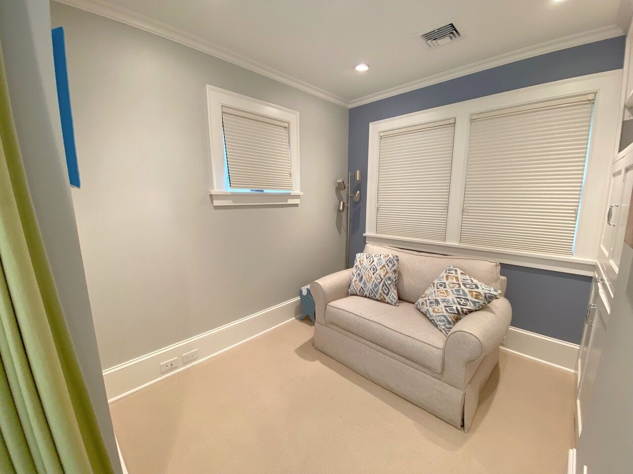 A room with a beige sofa, two patterned pillows, and a window with blinds.