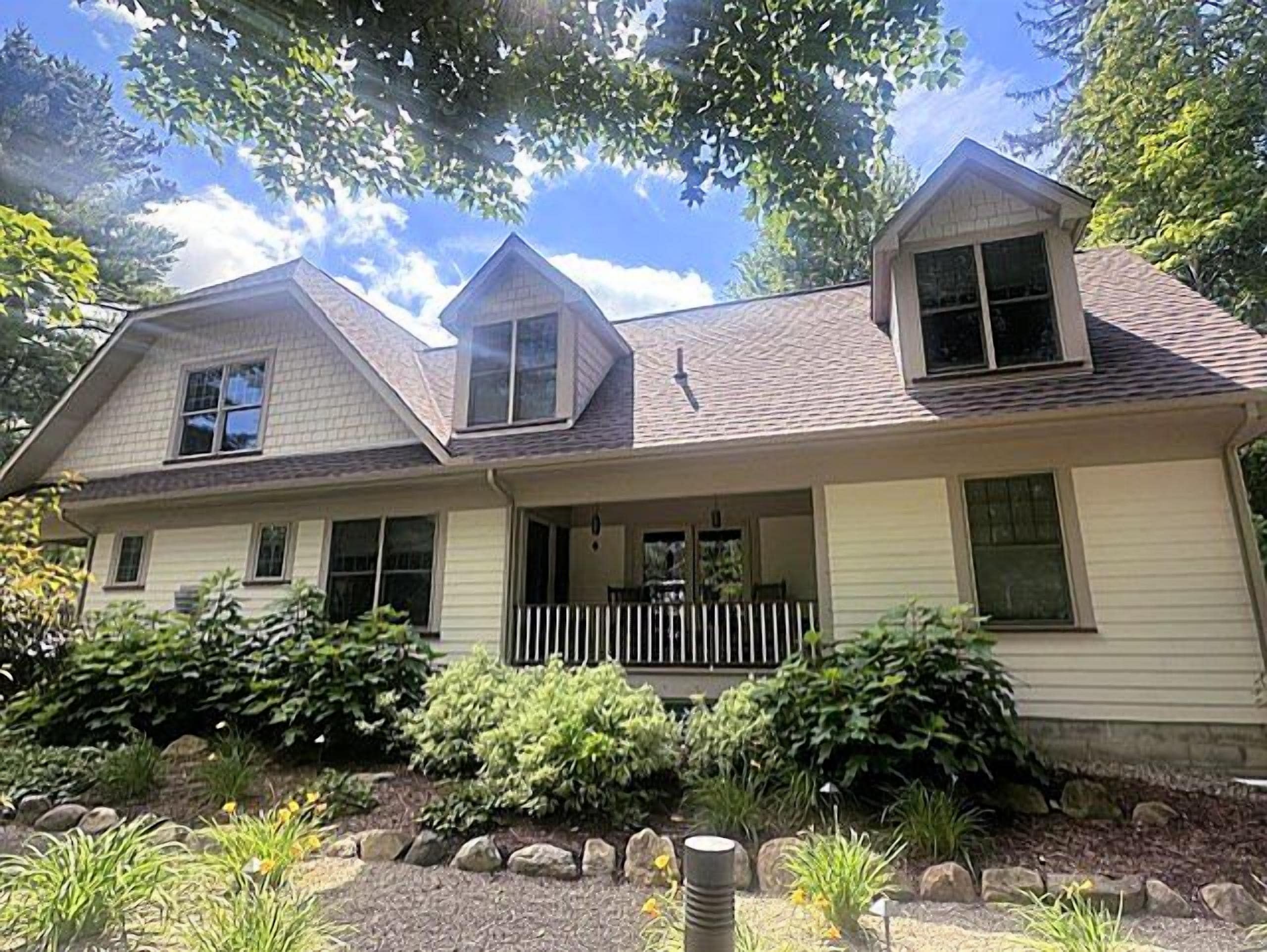 A two-story house with a front porch, a small attached garage, and a landscaped front yard with various plants and a stone pathway.