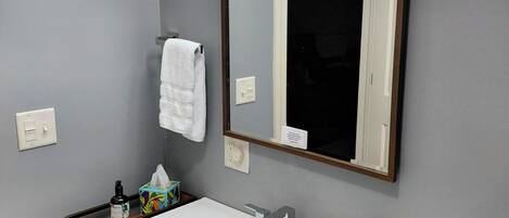 A bathroom with a white sink, wooden vanity, a mirror with lights, and a towel hanging on the wall.