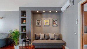 Un salon moderne avec un canapé gris, une petite table d’appoint, une plante en pot et un climatiseur fixé au mur.