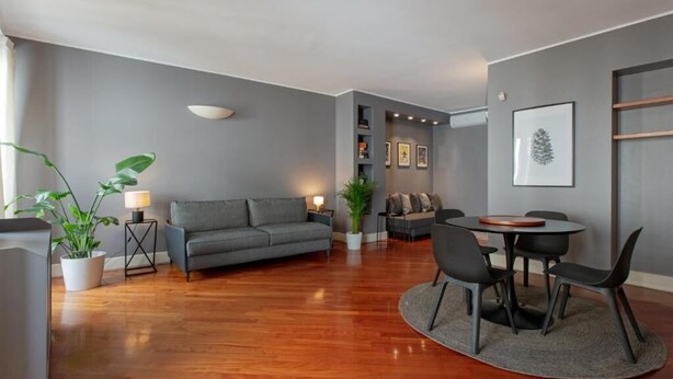 Un salon moderne avec un canapé gris, une table à manger avec des chaises et une plante en pot.