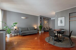 A modern living room with a grey sofa, a dining table with chairs, and a potted plant. - Penthouse on Domplatz, sleeps 6 (Milano)