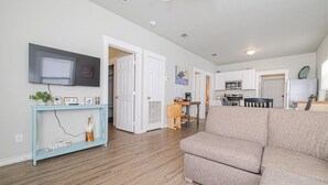 Ein Wohnzimmer mit einem beige gefärbten Sofa, einem hellblauen Konsolentisch mit Dekorationen, einem flachbildfernseher, der an der Wand angebracht ist, und einem Holzboden.