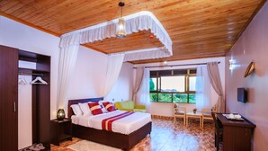 A bedroom with a wooden ceiling, a bed with white bedding and red pillows, a bedside table with a lamp, and a window with curtains. - victoria view boutique hotels and tours (Kampala)