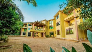 A yellow multi-story building with a covered central courtyard, surrounded by greenery. - victoria view boutique hotels and tours (Kampala)