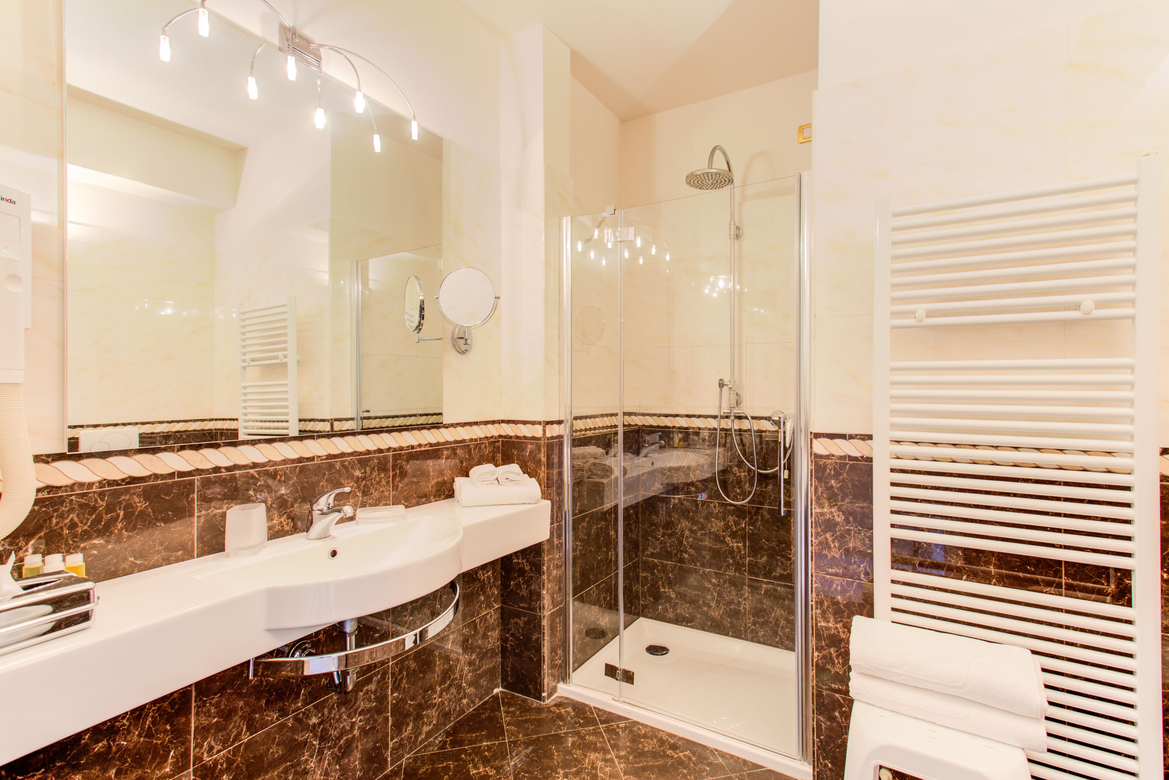 Un baño moderno con ducha de vidrio, un espejo grande y un lavamanos blanco.