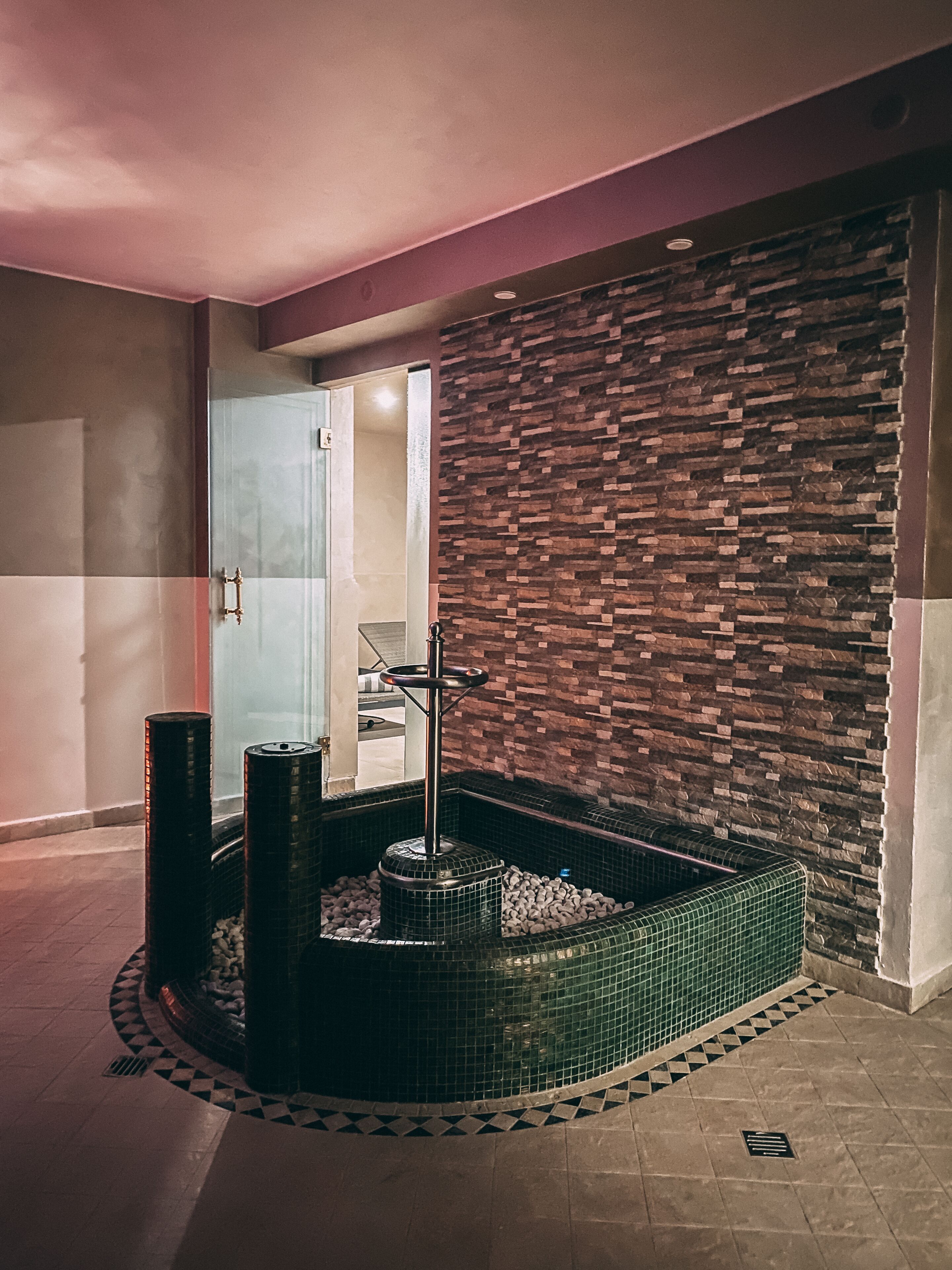 A spa area with a stone wall, a hot tub, and a glass door leading to a room.