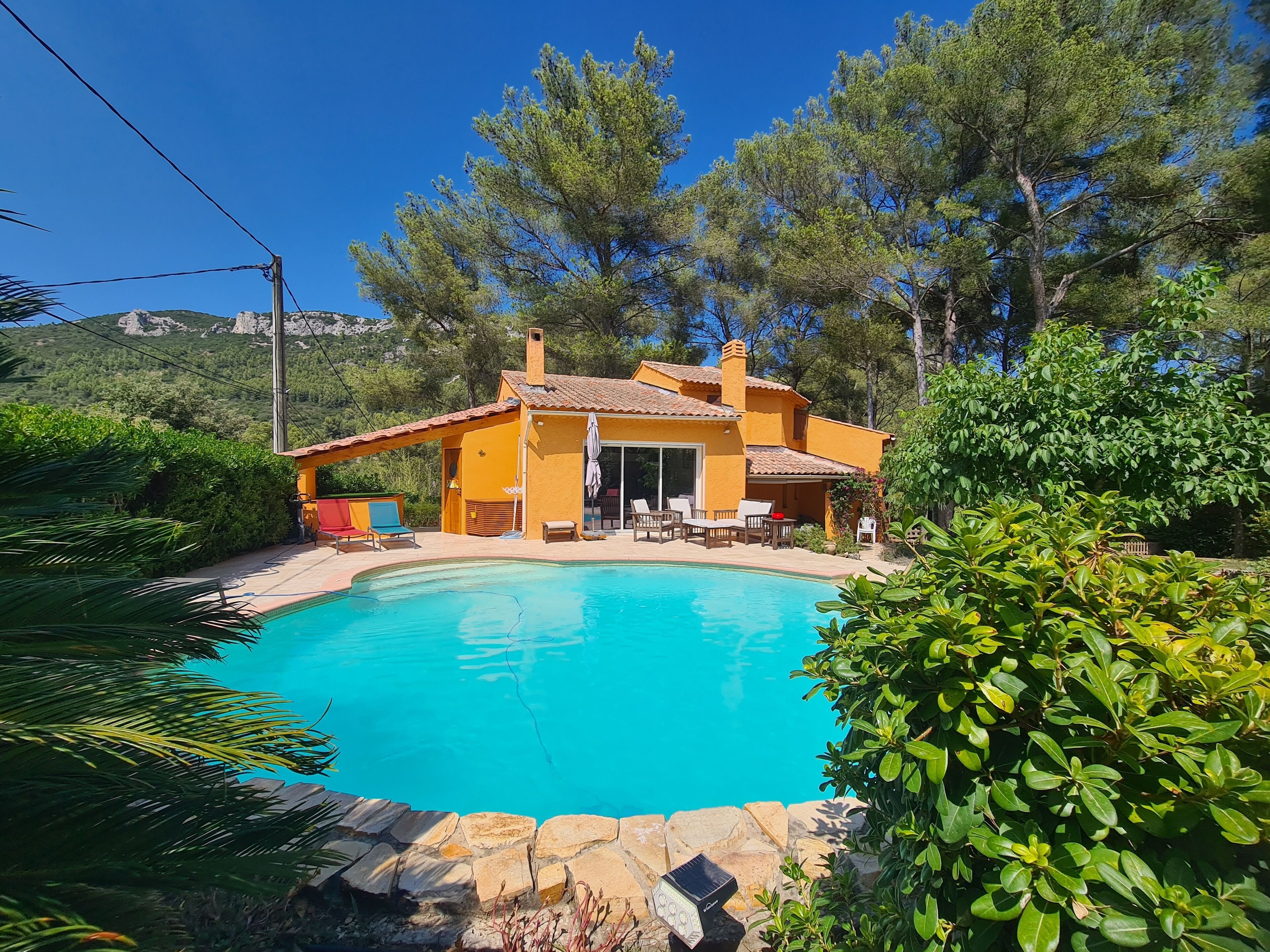 Ein Haus mit Schwimmbad, umgeben von Grün und einer Hügelkulisse im Hintergrund.