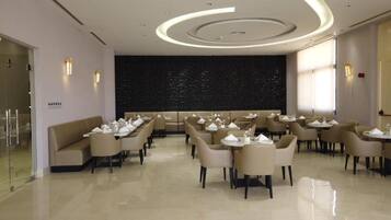 Un restaurante moderno con mesas redondas y sillas color beige, una pared de mármol oscuro e iluminación empotrada.