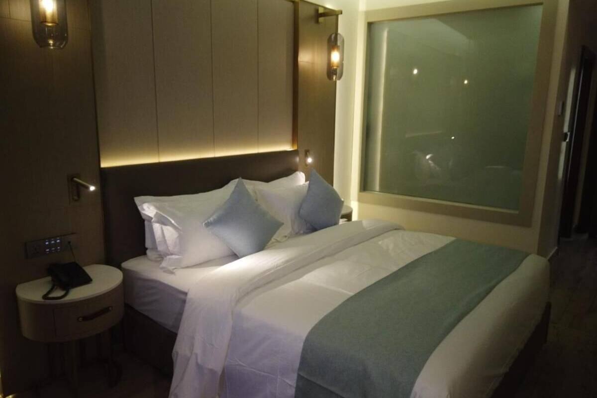 A hotel room with a bed, bedside table, and a large window.