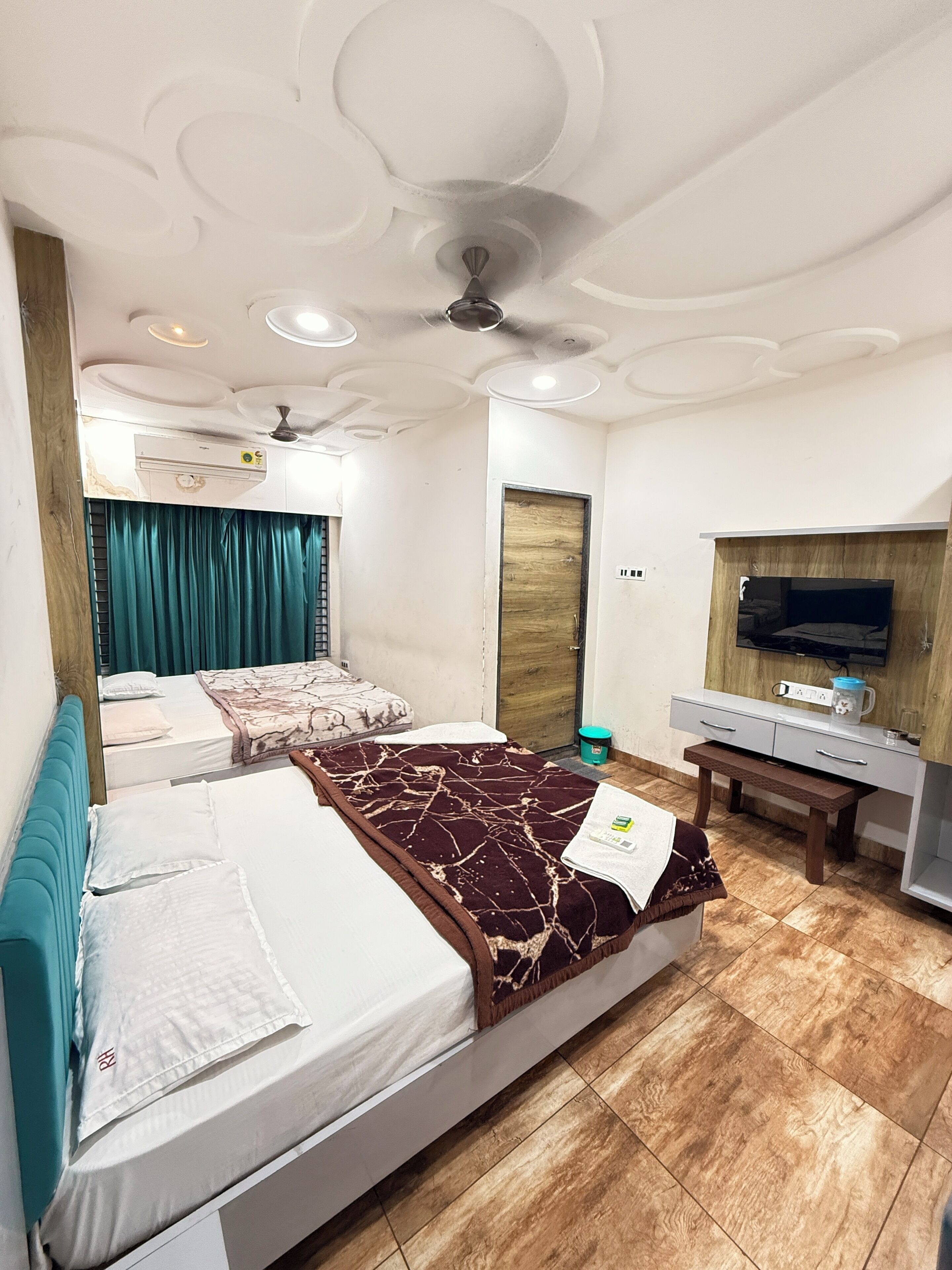 A hotel room with two beds, a TV, a desk, and a ceiling fan.