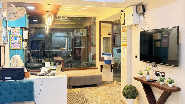A modern living room with a sofa, a coffee table, a TV mounted on the wall, and a ceiling fan. - Hotel Raghuveera Palace (Ujjain)