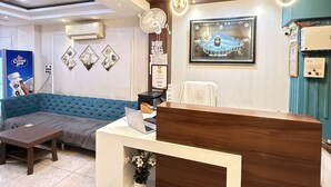 A reception area with a wooden desk, a blue sofa, and a framed picture on the wall. - Hotel Raghuveera Palace (Ujjain)