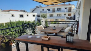 An outdoor balcony with a wooden table, two chairs, and a potted plant. - Paramount Gardens Resorts C201 (Tersefanou)